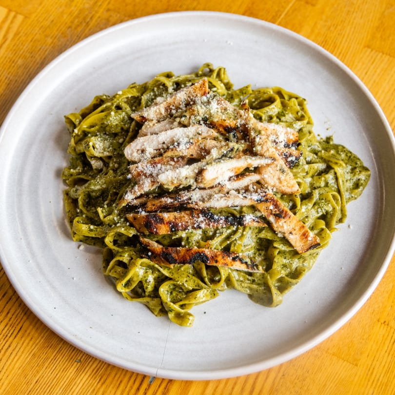 Fettuccine pasta with green pesto sauce, grilled chicken, and Parmesan cheese.