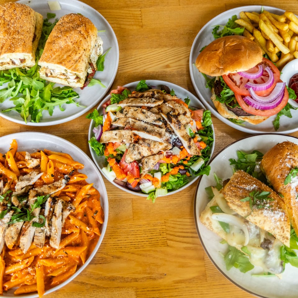 Various restaurant dishes: chicken subs, a burger with fries, grilled chicken salad, and penne pasta.