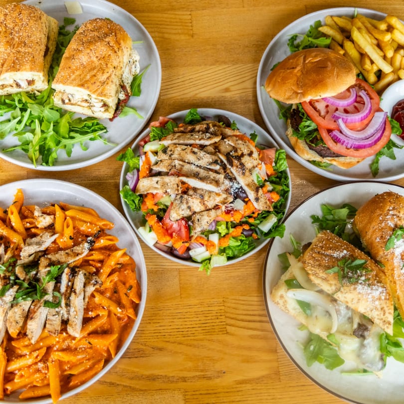 Various restaurant dishes: chicken subs, a burger with fries, grilled chicken salad, and penne pasta.