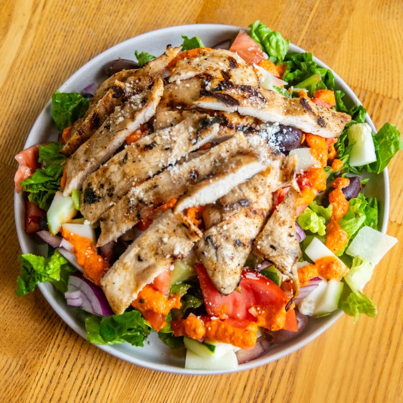 Grilled chicken salad with fresh greens, vegetables, orange dressing, and grated cheese.