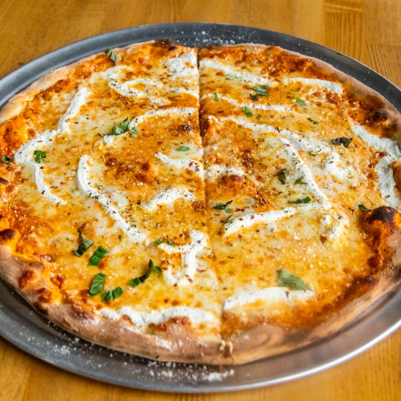 Round pizza with red sauce, mozzarella, ricotta swirls, and fresh basil, sliced on a metal tray.