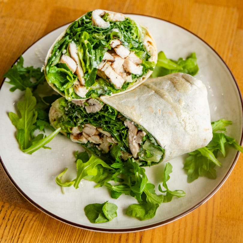 Chicken Caesar wrap, cut in half, on a plate with arugula garnish.