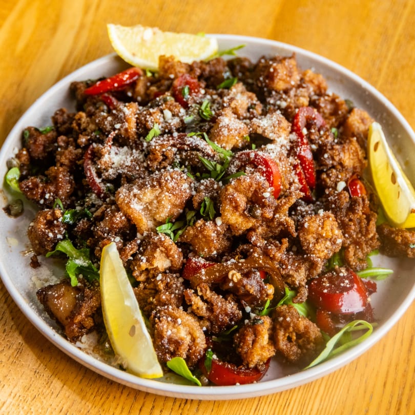 Plate of crispy fried calamari with lemon, red peppers, herbs, and grated cheese.