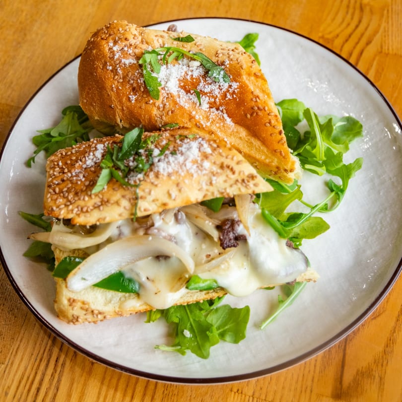 Melted cheese sub sandwich with sautéed onions, green peppers, and arugula on a sesame bun.