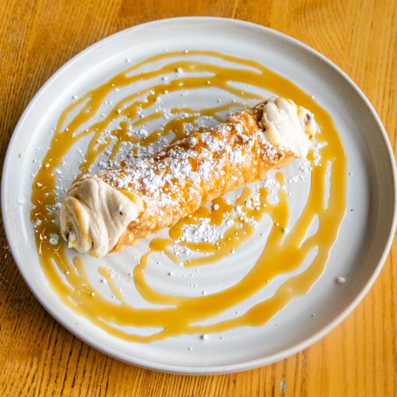 Golden-brown cannoli filled with cream, dusted with powdered sugar and caramel sauce on a white plate.