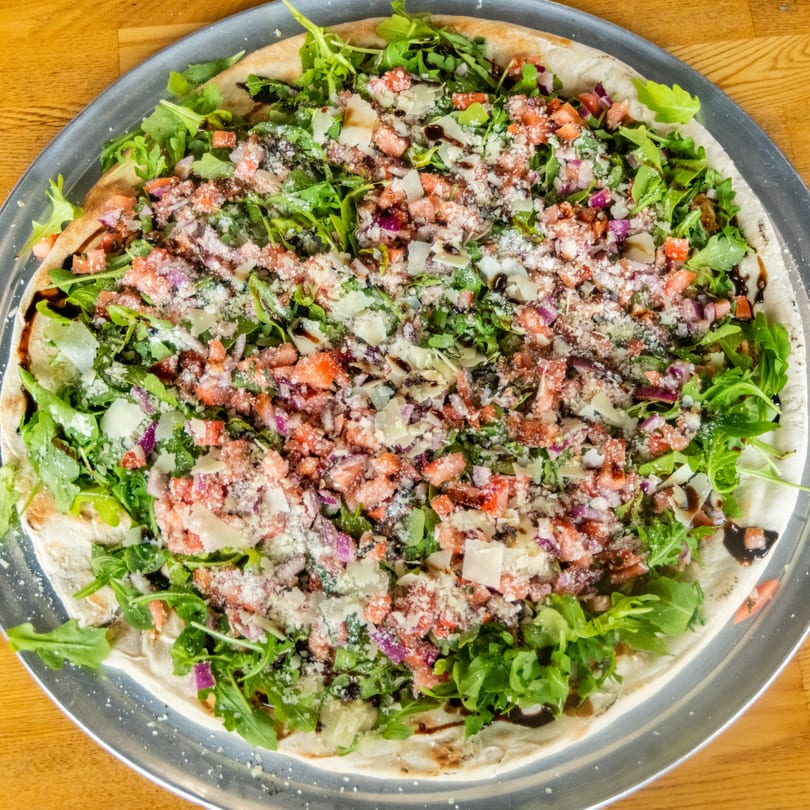 Pizza topped with fresh arugula, diced tomatoes, red onions, parmesan, and balsamic glaze.