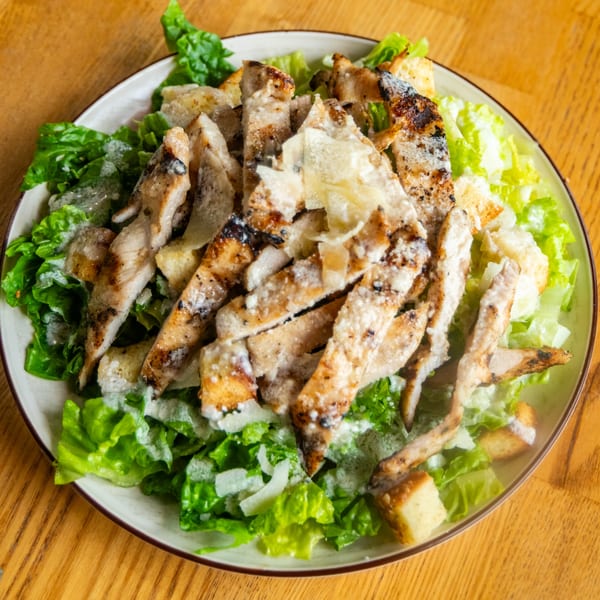 Fresh Caesar salad topped with sliced grilled chicken, croutons, and shaved parmesan cheese.