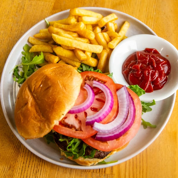 Open-faced burger with tomato, red onion, lettuce, golden fries, and ketchup on a plate.