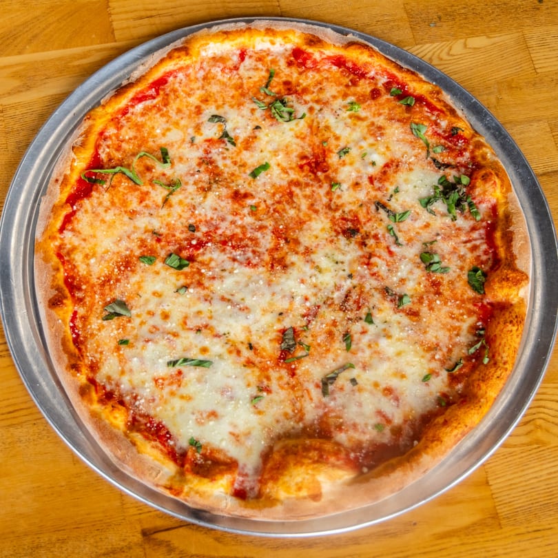 Classic cheese pizza with tomato sauce, melted mozzarella, fresh basil, and parmesan on a metal tray.