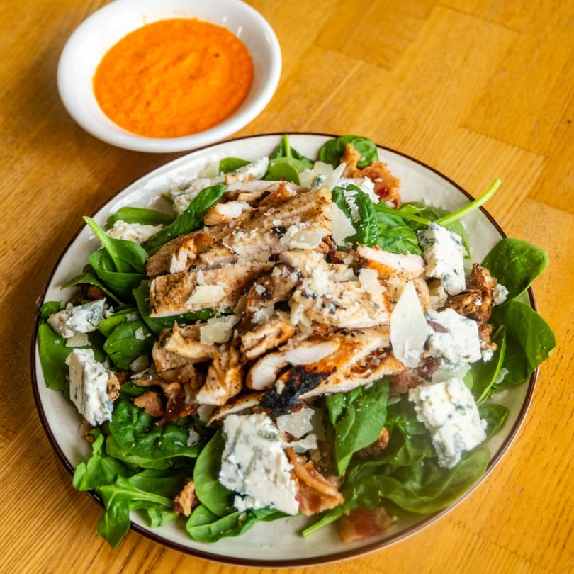 A vibrant salad with grilled chicken, fresh spinach, blue cheese, and a side of orange dressing.