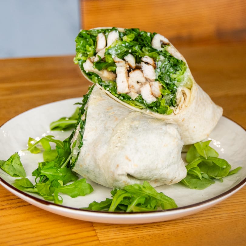 Halved chicken wrap with grilled chicken, fresh greens, and creamy dressing on a white plate.