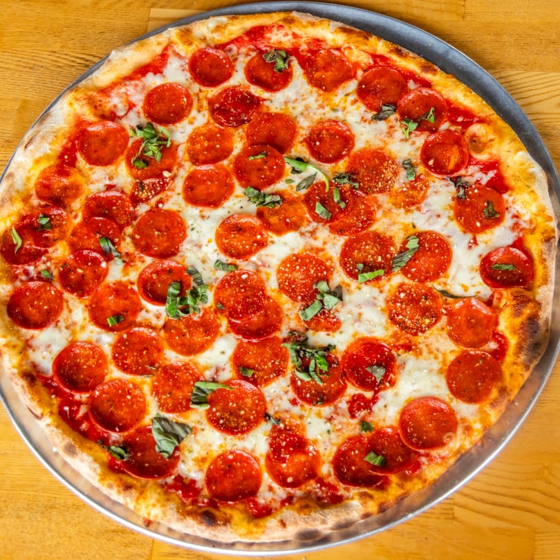 Round pepperoni pizza with melted cheese, red sauce, and fresh basil on a metal pan.